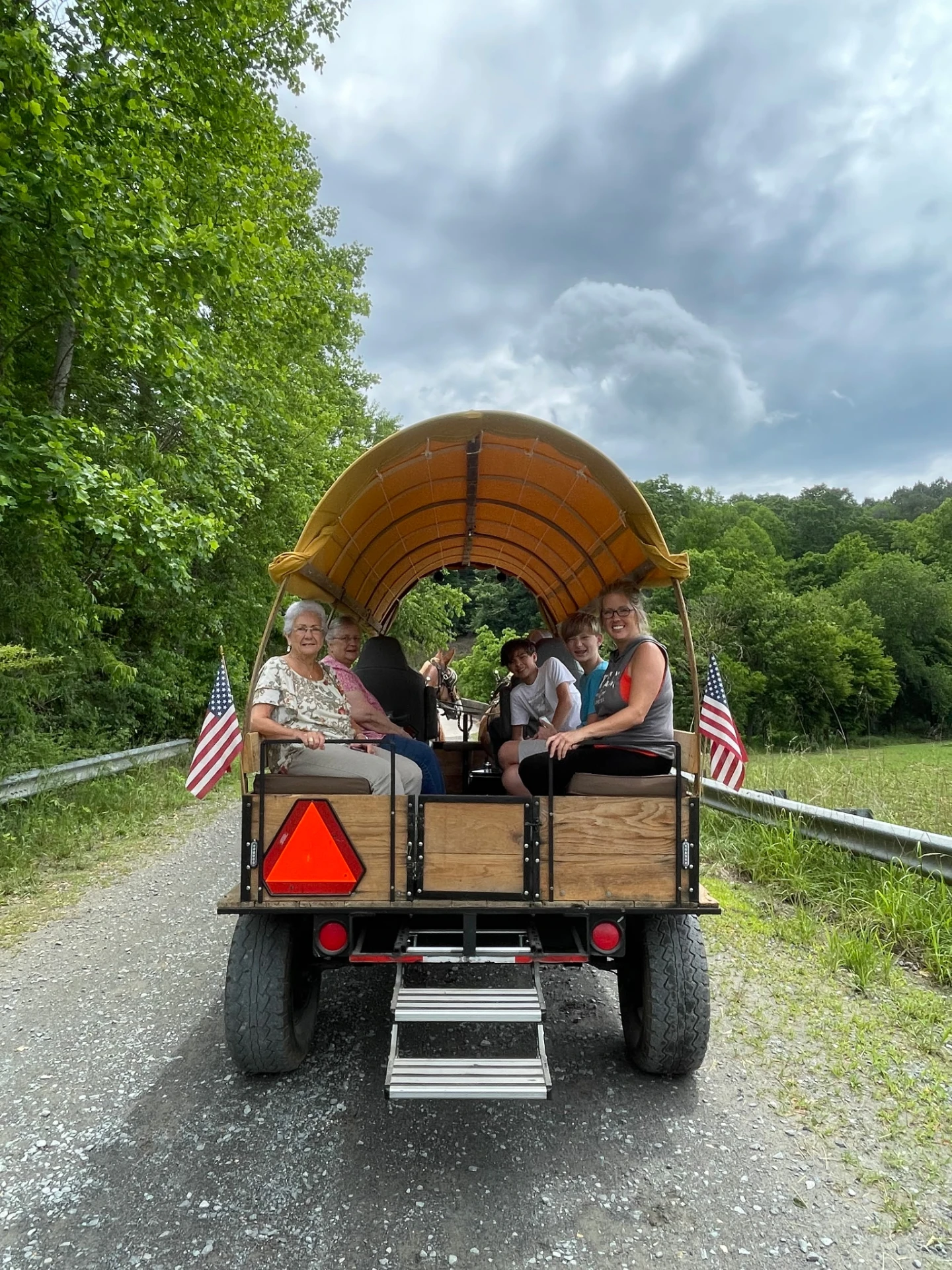 A family riding together in the canopy wagon on a wooded gravel road