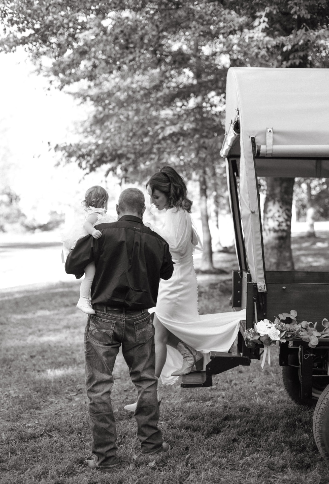 Black-and-white photo of a bride stepping up into the flower-trimmed wagon on her wedding day